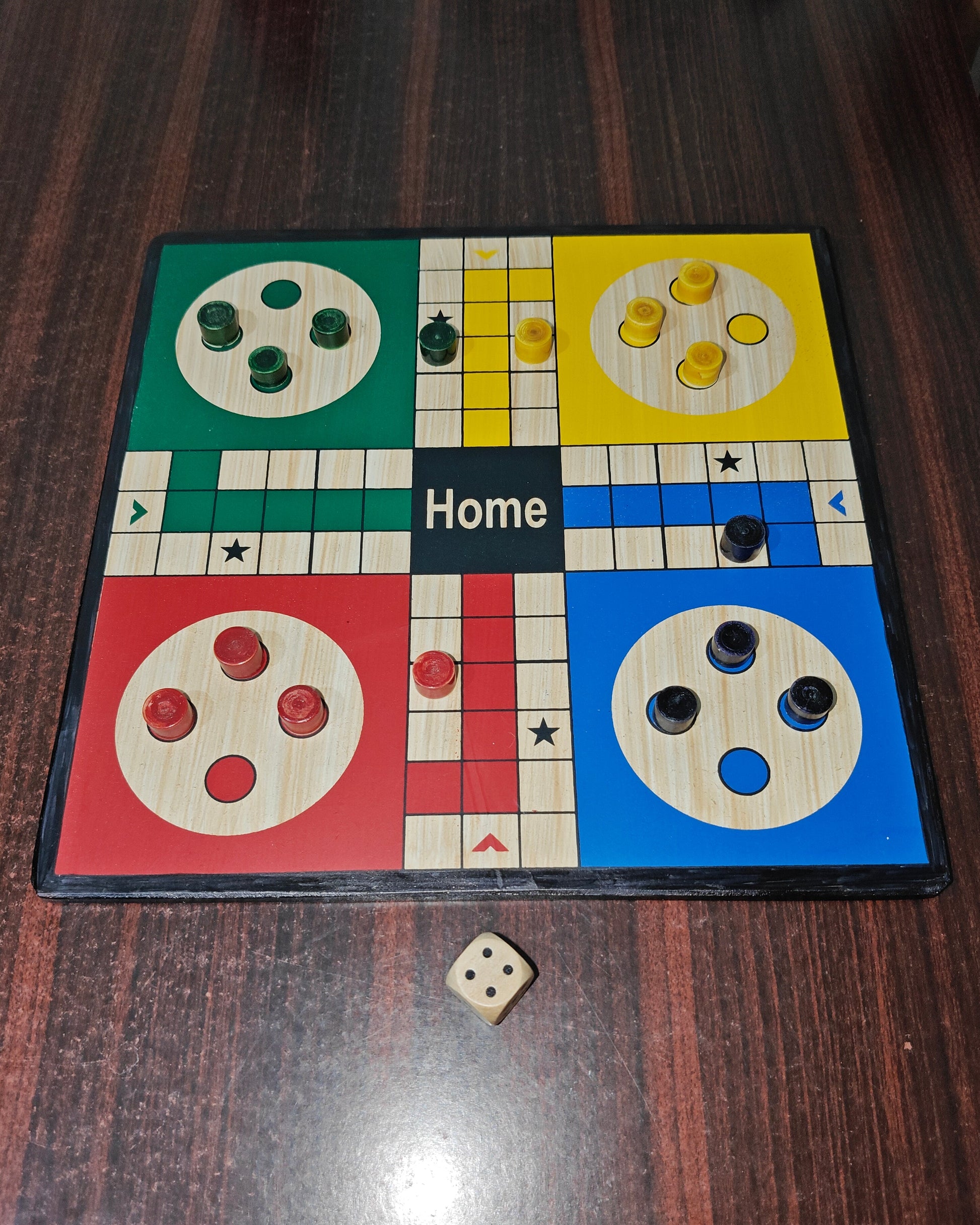 Ludo board game on a wooden surface with pieces and a dice.